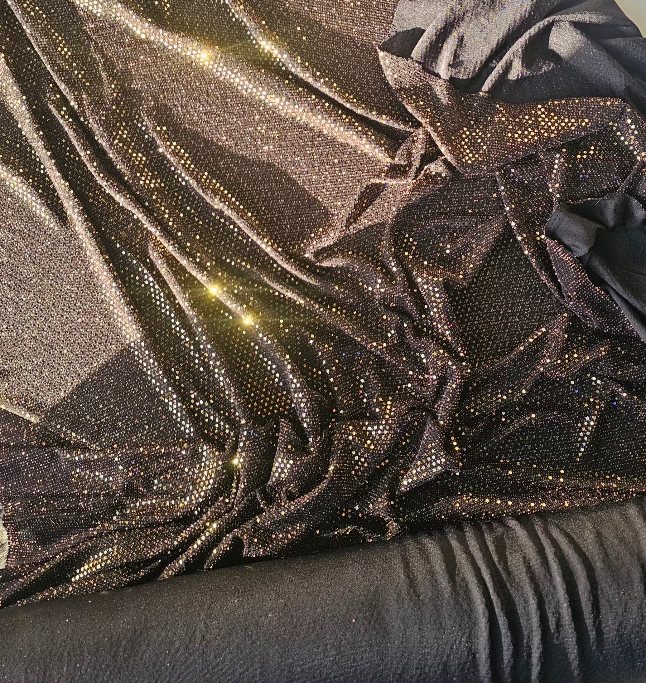 Shimmering sequin fabric in a dark bronze-brown color, draped and folded to show its reflective texture and glittering details.