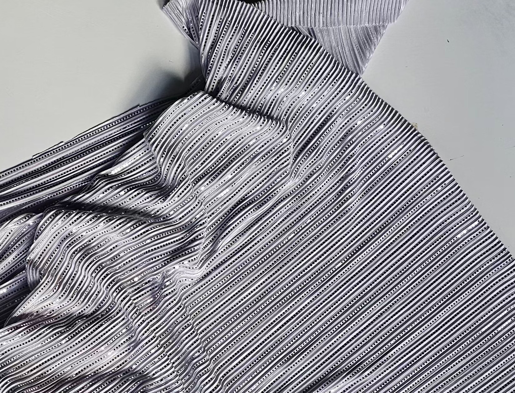 A crumpled piece of gray and white striped fabric with a subtle sheen, laid out on a light gray background.