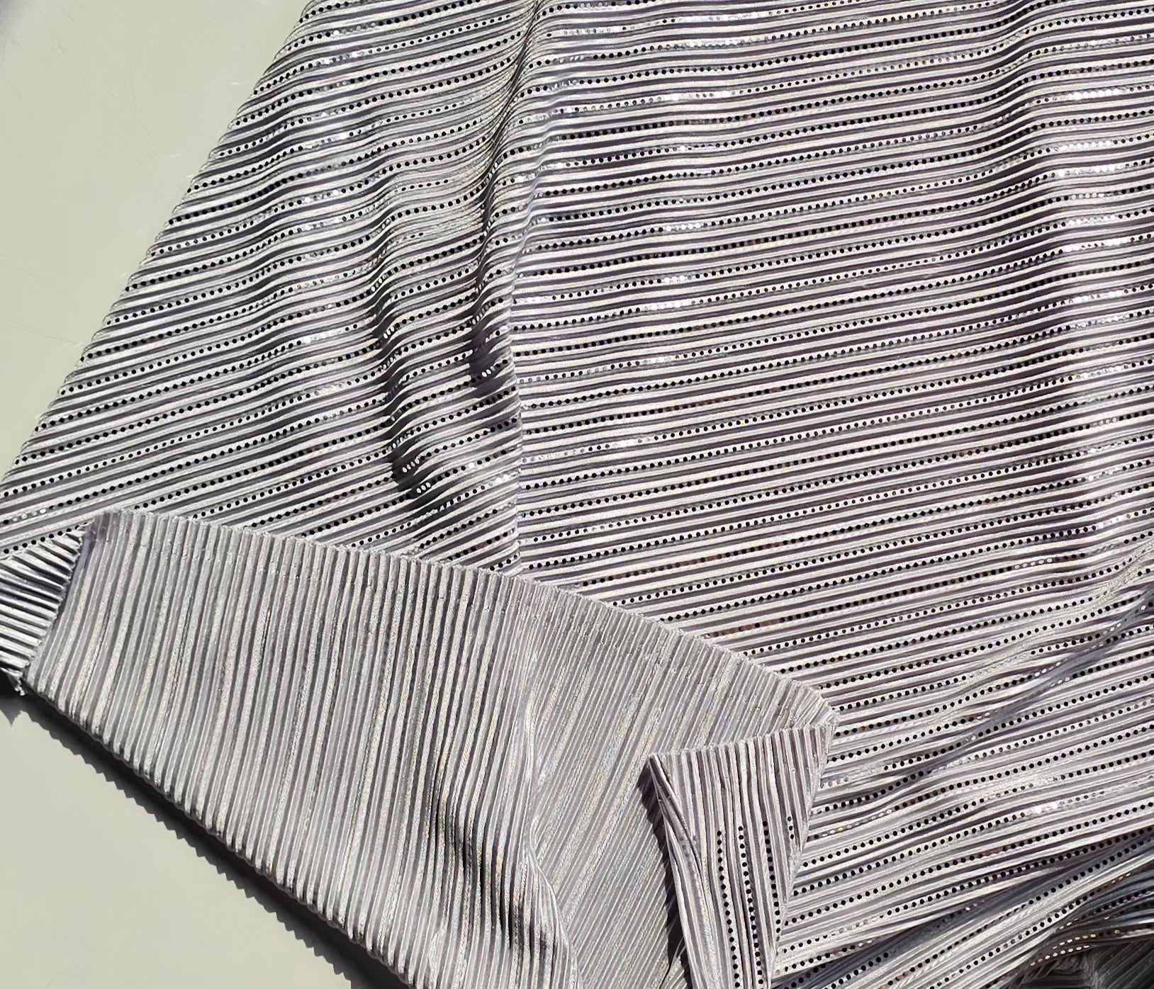 A close-up of a gray and white striped fabric with a fine vertical stripe pattern and small dotted horizontal accents, folded to show texture and color.
