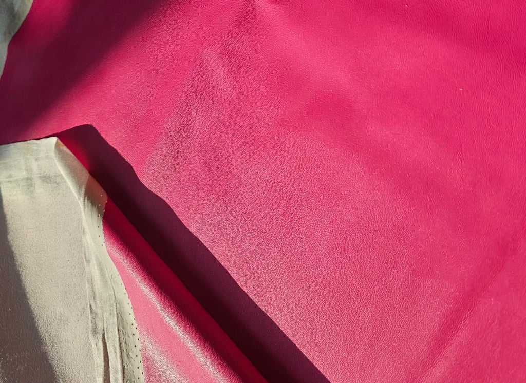 A close-up of bright pink fabric with a folded section showing a contrasting dark magenta underside, photographed against a white background.