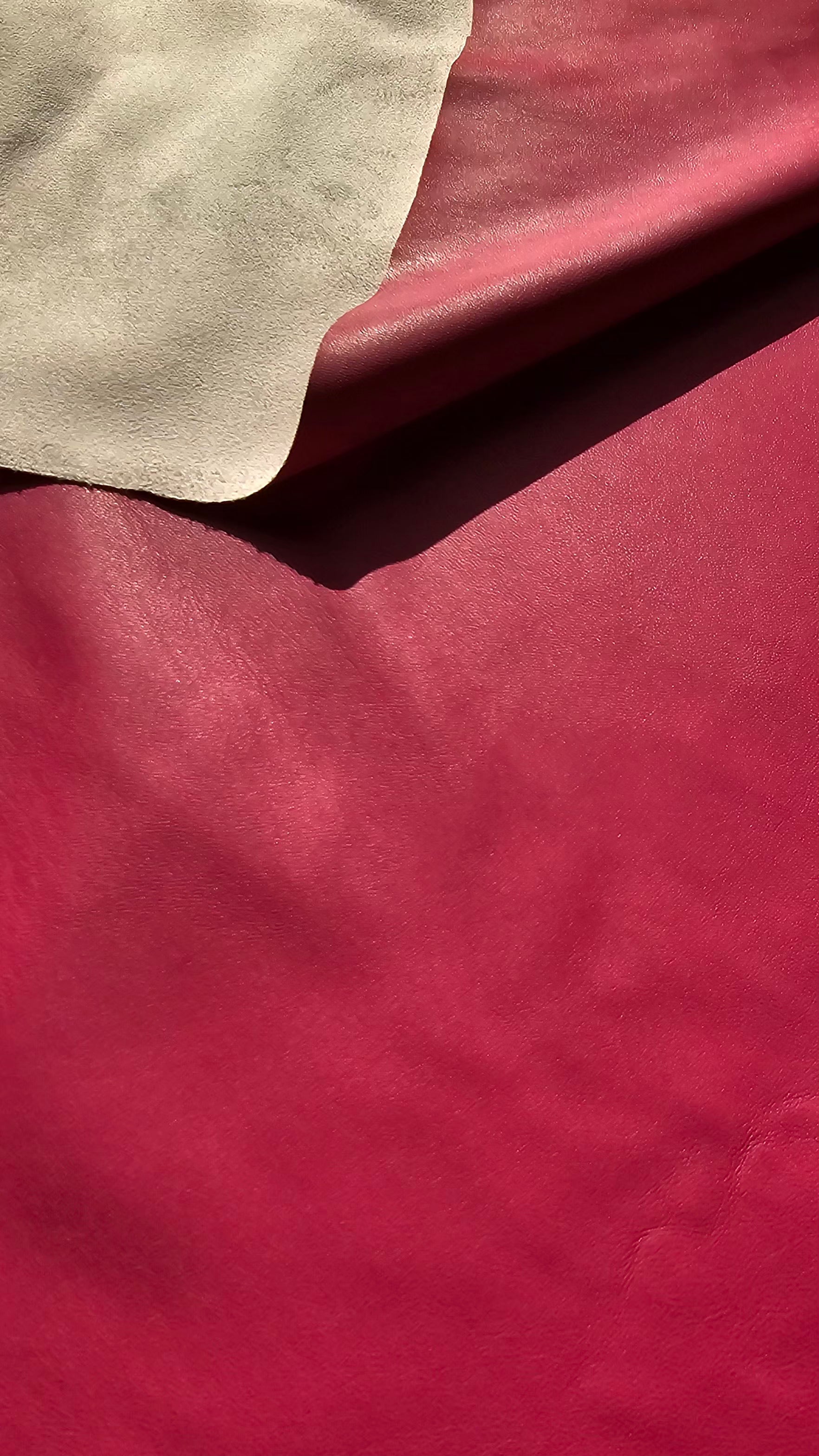 A close-up of a deep red leather material with a folded corner revealing a light beige underside.