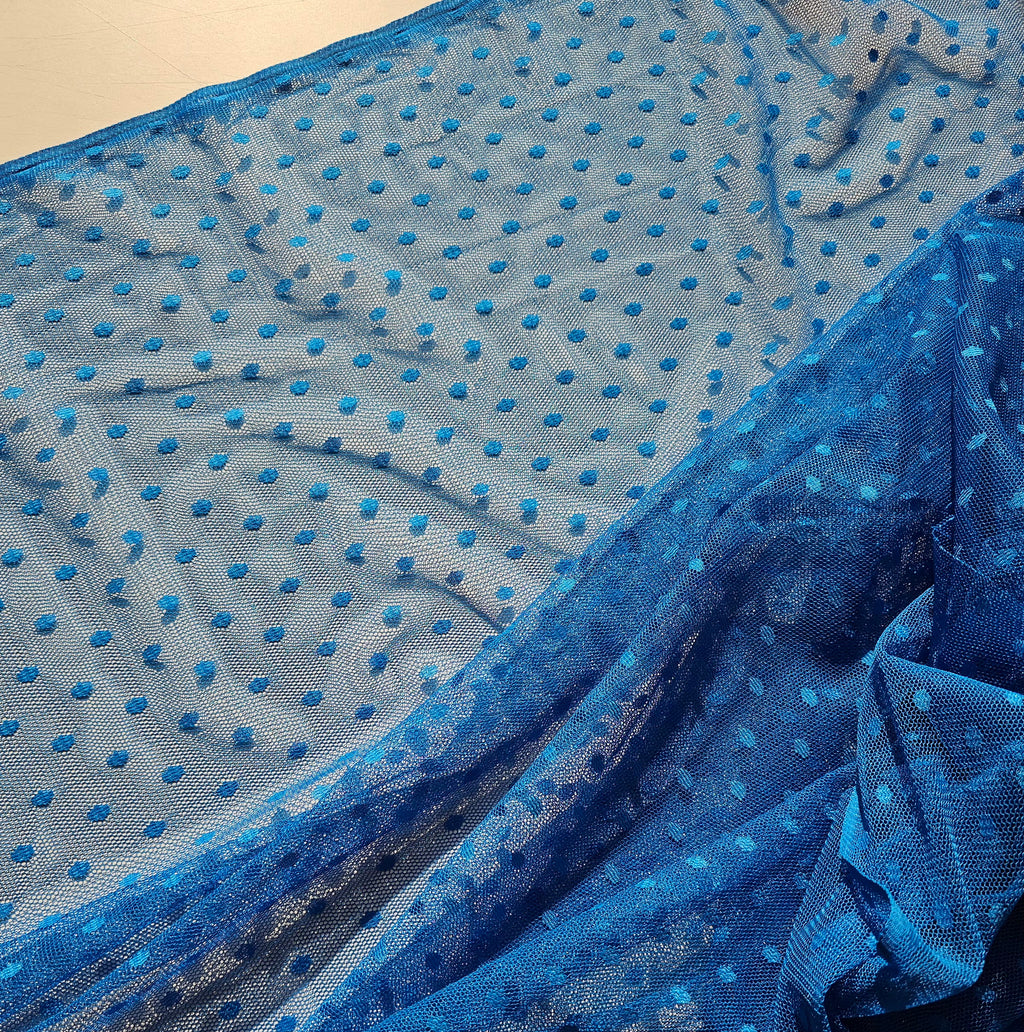 Blue sheer mesh fabric with a repeating pattern of raised blue polka dots, draped to show its texture and transparency.