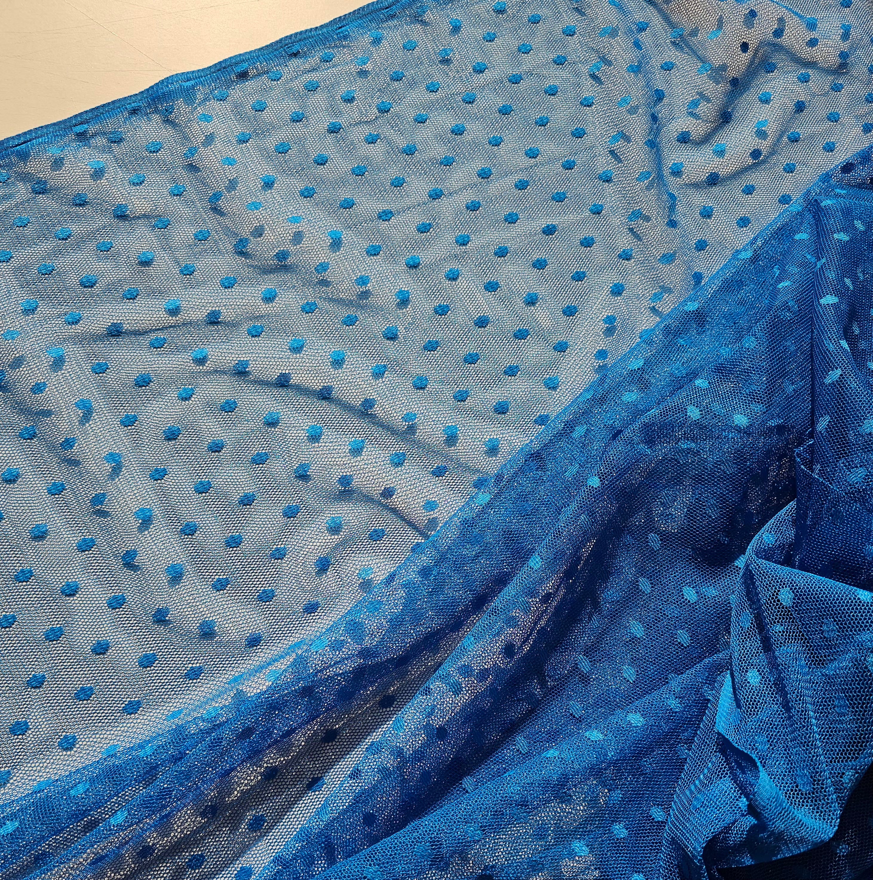 Blue sheer mesh fabric with a repeating pattern of raised blue polka dots, draped to show its texture and transparency.