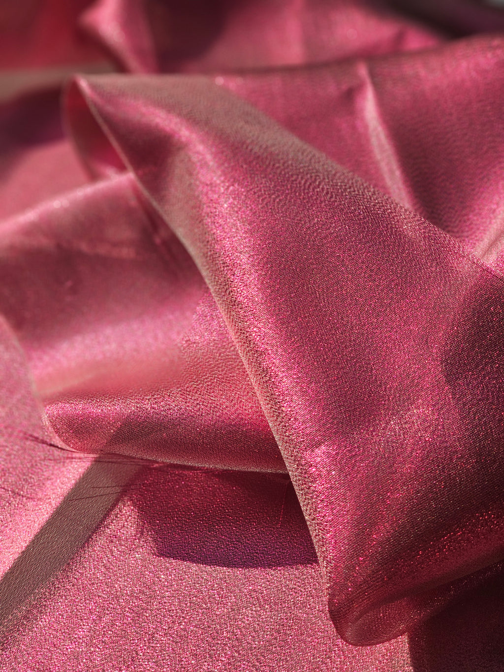 A close-up of draped pink fabric with a subtle sheen and fine texture, filling the frame.