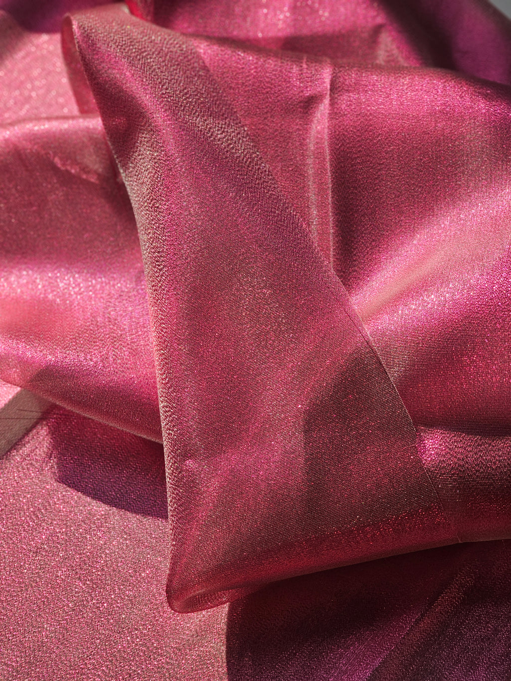 A close-up of draped pink fabric with a subtle sheen and fine texture, folded to show its lustrous surface.