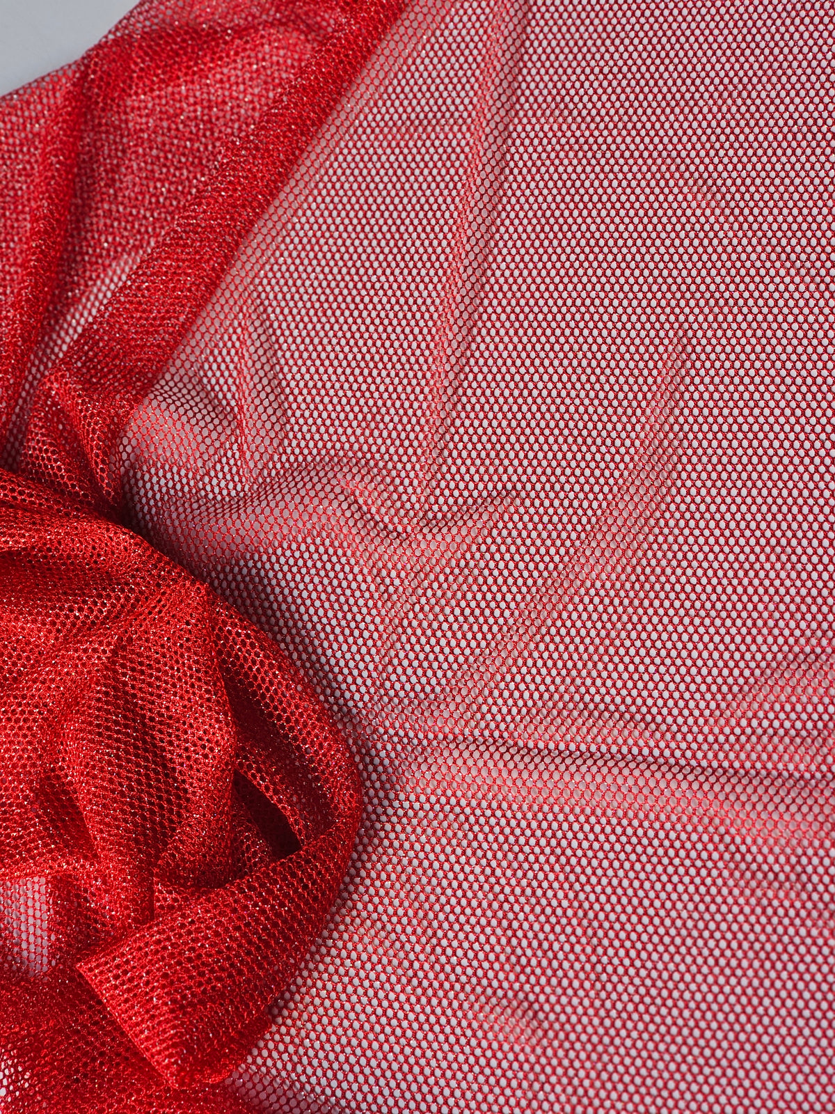 A close-up of red mesh fabric with a fine woven pattern, draped and folded to show texture and transparency.