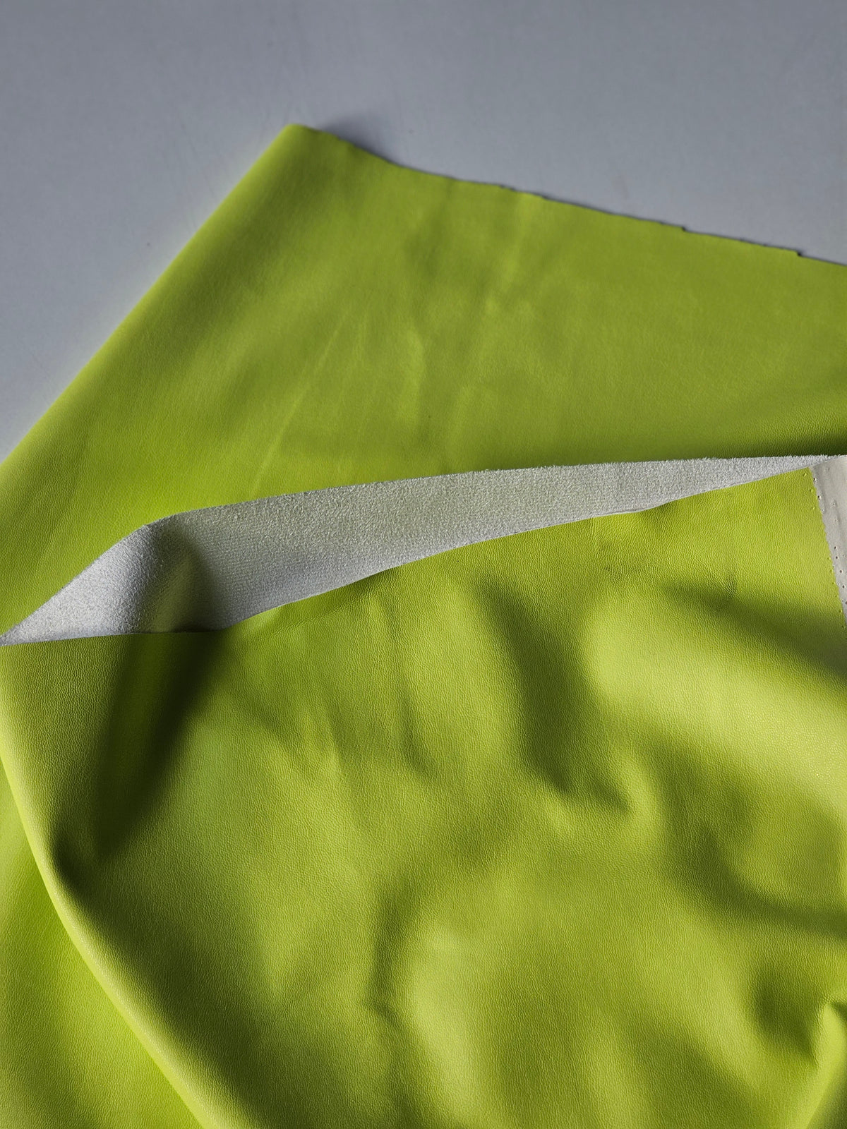 A close-up of a bright lime green fabric, showing its smooth texture and a contrasting white inner lining folded over.