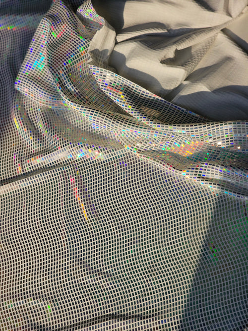 A close-up of shimmering holographic mesh fabric draped in soft folds, showing an iridescent rainbow sheen over a light gray base.