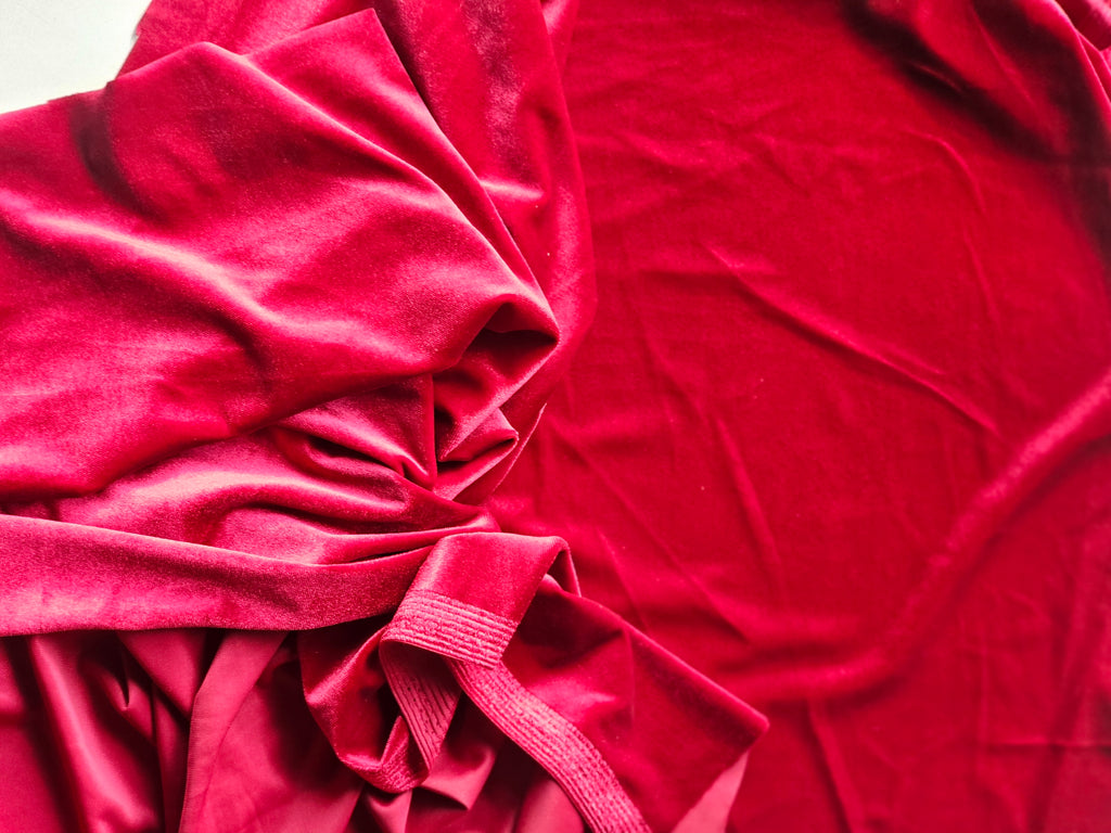 A close-up of draped red velvet fabric with soft folds and a gathered tie at the bottom left, filling the frame.