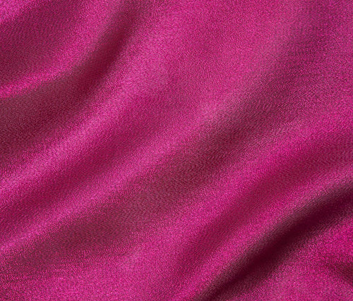 A close-up of draped magenta pink fabric with soft folds and a smooth texture.