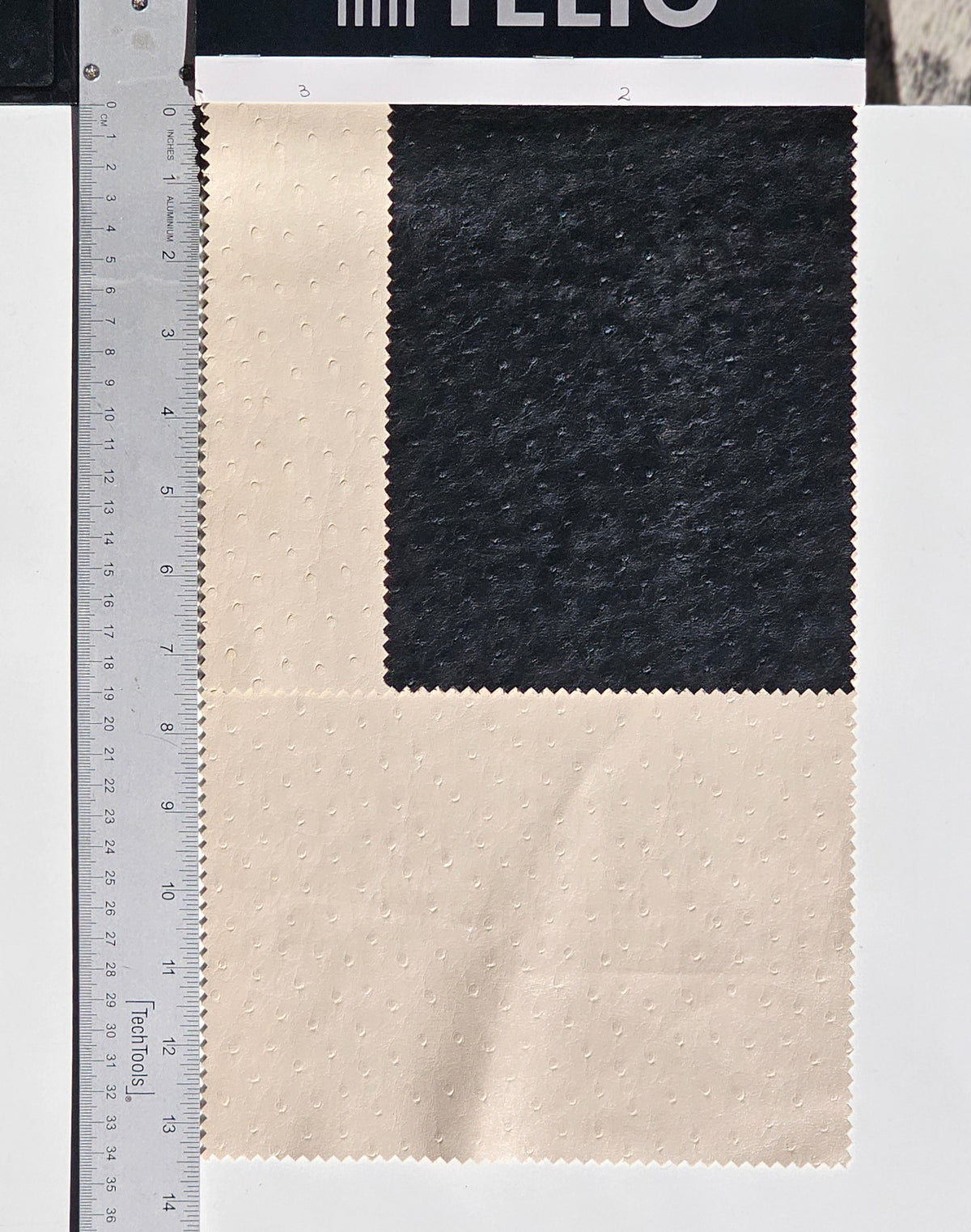 Two textured fabric swatches, one black and one cream, shown next to a metal ruler for scale on a white background.