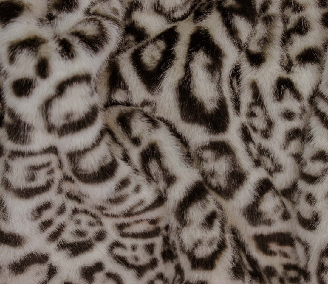 Close-up of a faux fur fabric with a leopard print pattern in black, gray, and cream.
