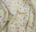 Close-up of a soft plush fabric in off-white with scattered small multicolored confetti dots in yellow, blue, pink, and orange.