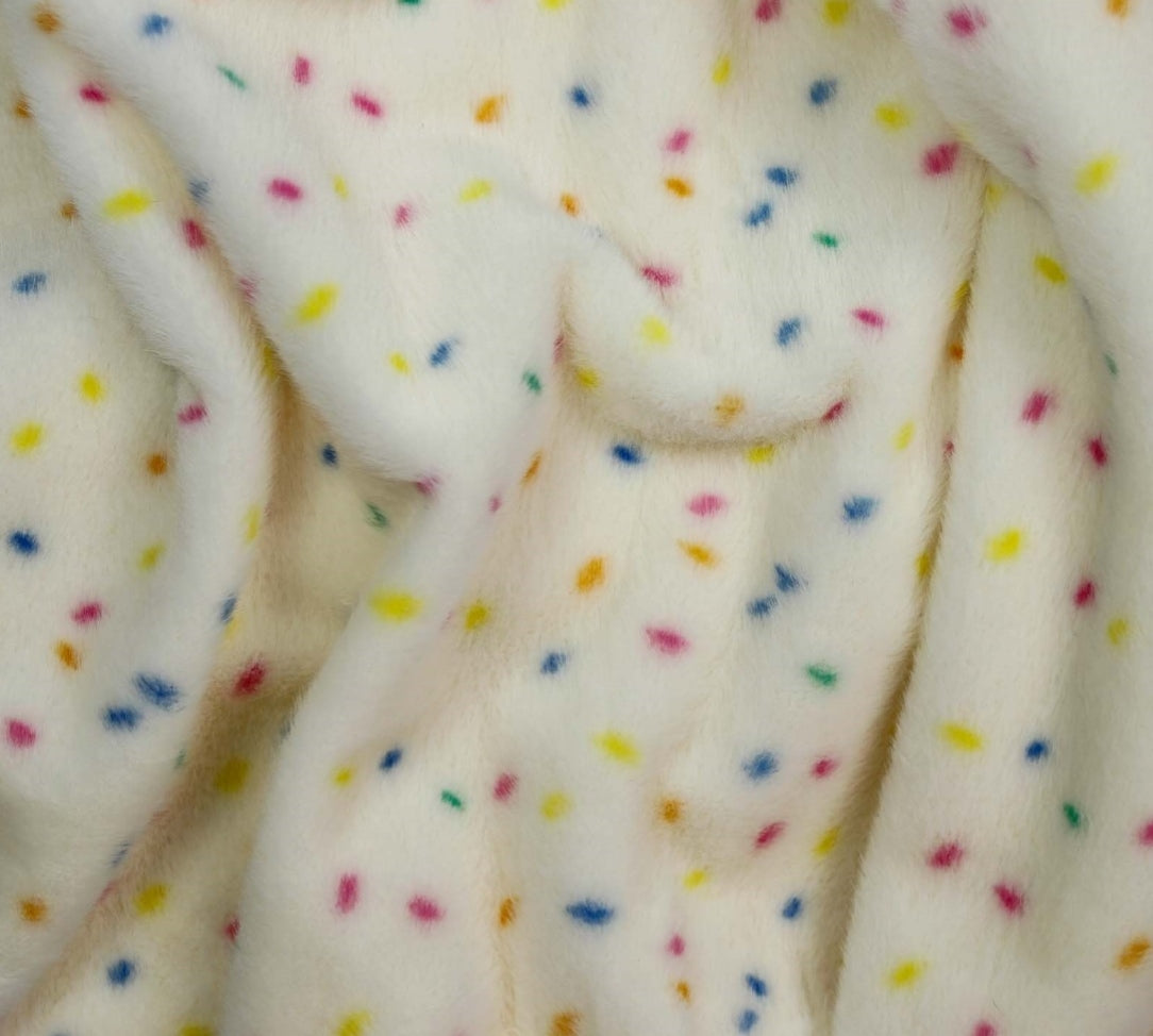 Close-up of a soft plush fabric in off-white with scattered small multicolored confetti dots in yellow, blue, pink, and orange.